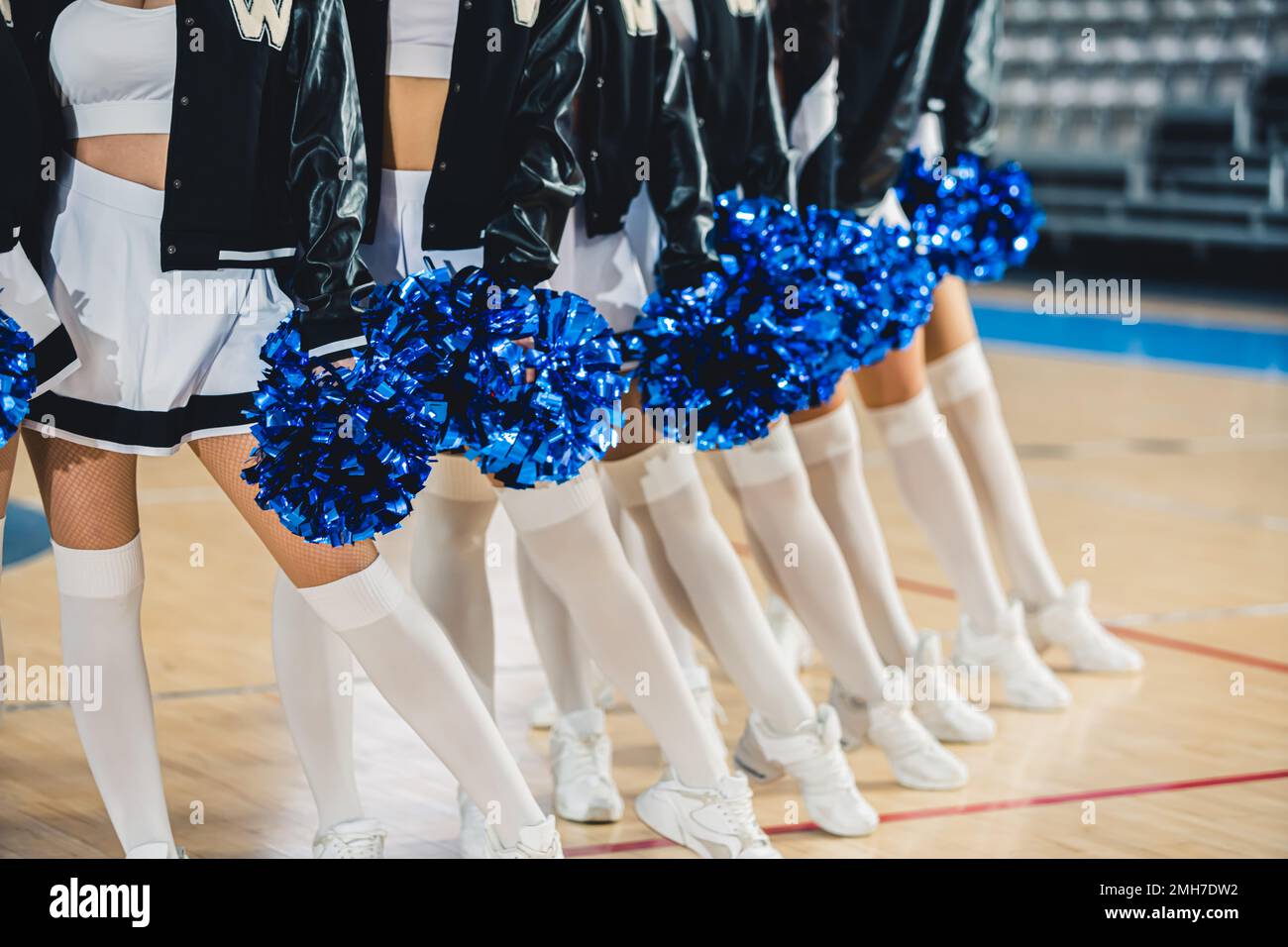 Mittellanger Volltreffer von Cheerleader in weißen Strümpfen und Schuhen, die sich in einer Reihe mit blauen Pompoms in den Händen posieren. Hochwertiges Foto Stockfoto