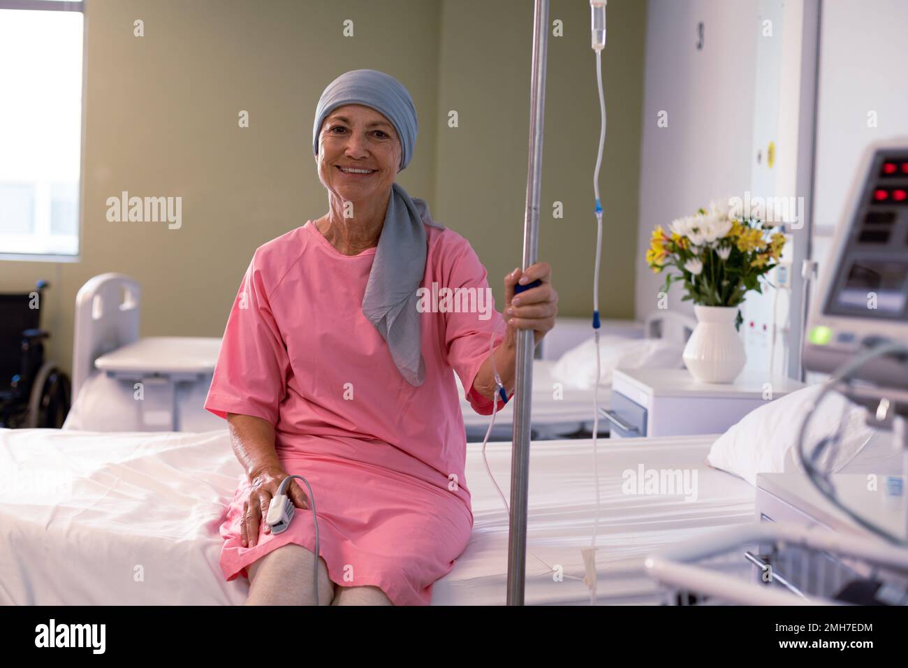 Glückliche leitende weiße weibliche Krebspatientin trägt Kopftuch und sitzt  mit Tropf im Krankenhaus auf dem Bett Stockfotografie - Alamy