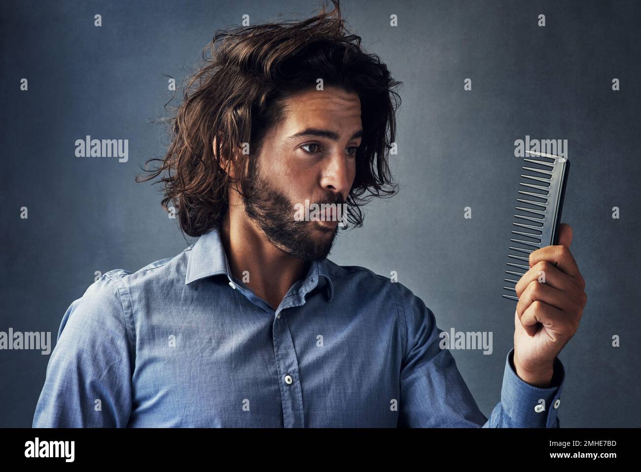 Ich hatte einen schlechten Tag. Studioaufnahme eines gutaussehenden jungen Mannes, der auf seinen Kamm blickt, während er sein Haar vor einem grauen Hintergrund bürstet. Stockfoto