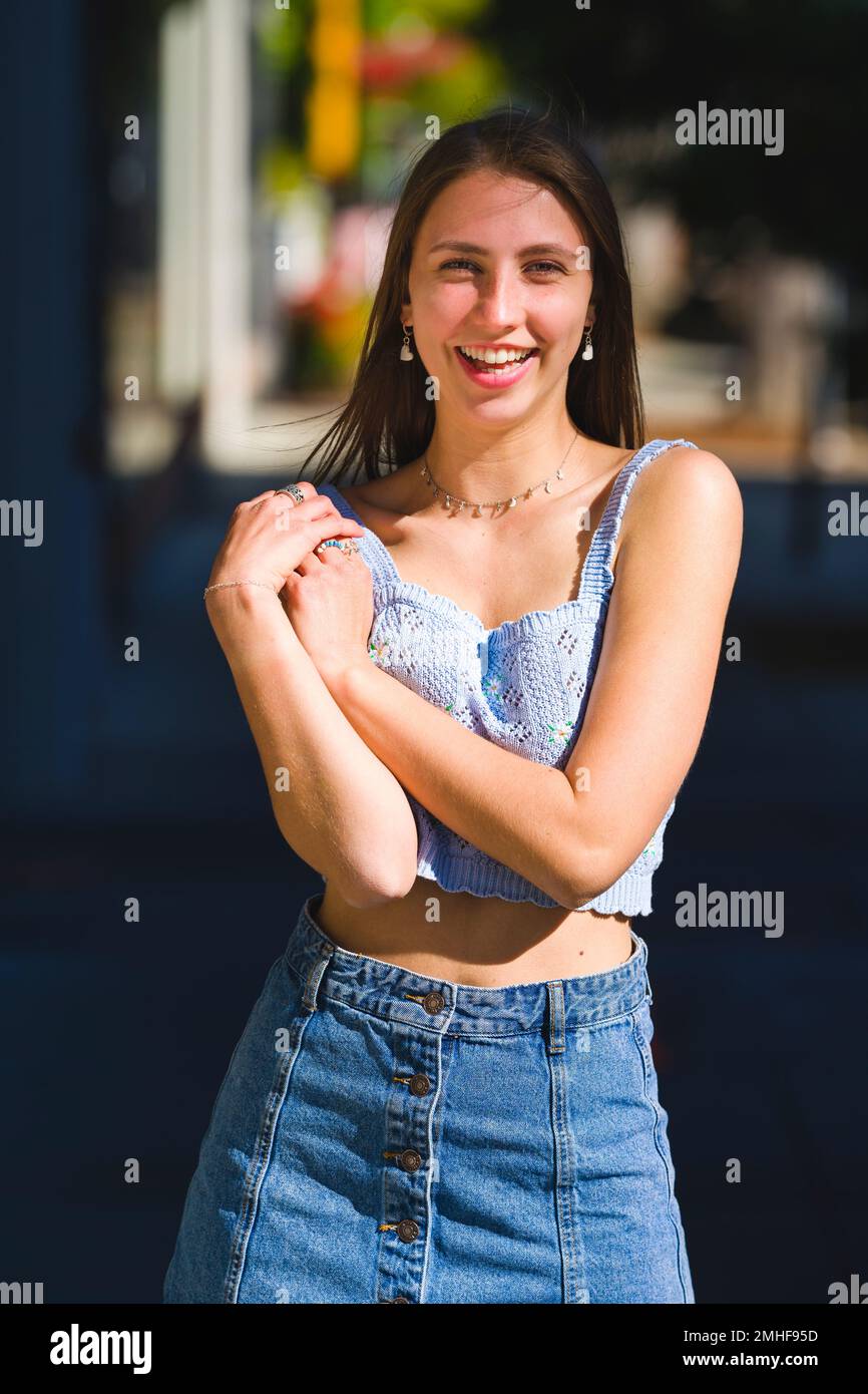 Hübsches lächelndes Mädchen im Teenageralter, das auf dem Bürgersteig von Downtown Palo Alto steht, gekleidet mit einem bauchfreien Oberteil im Sommer und einem kurzen Denim-Rock Stockfoto