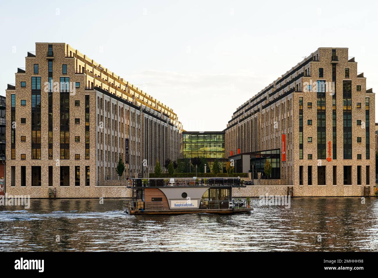Bürogebäude Cuvry Campus mit Lieferando Hauptquartier an der Spree, auf der ein Boot in der Nähe der Oberbaumbrücke in Berlin-Kreuzberg fährt. Stockfoto
