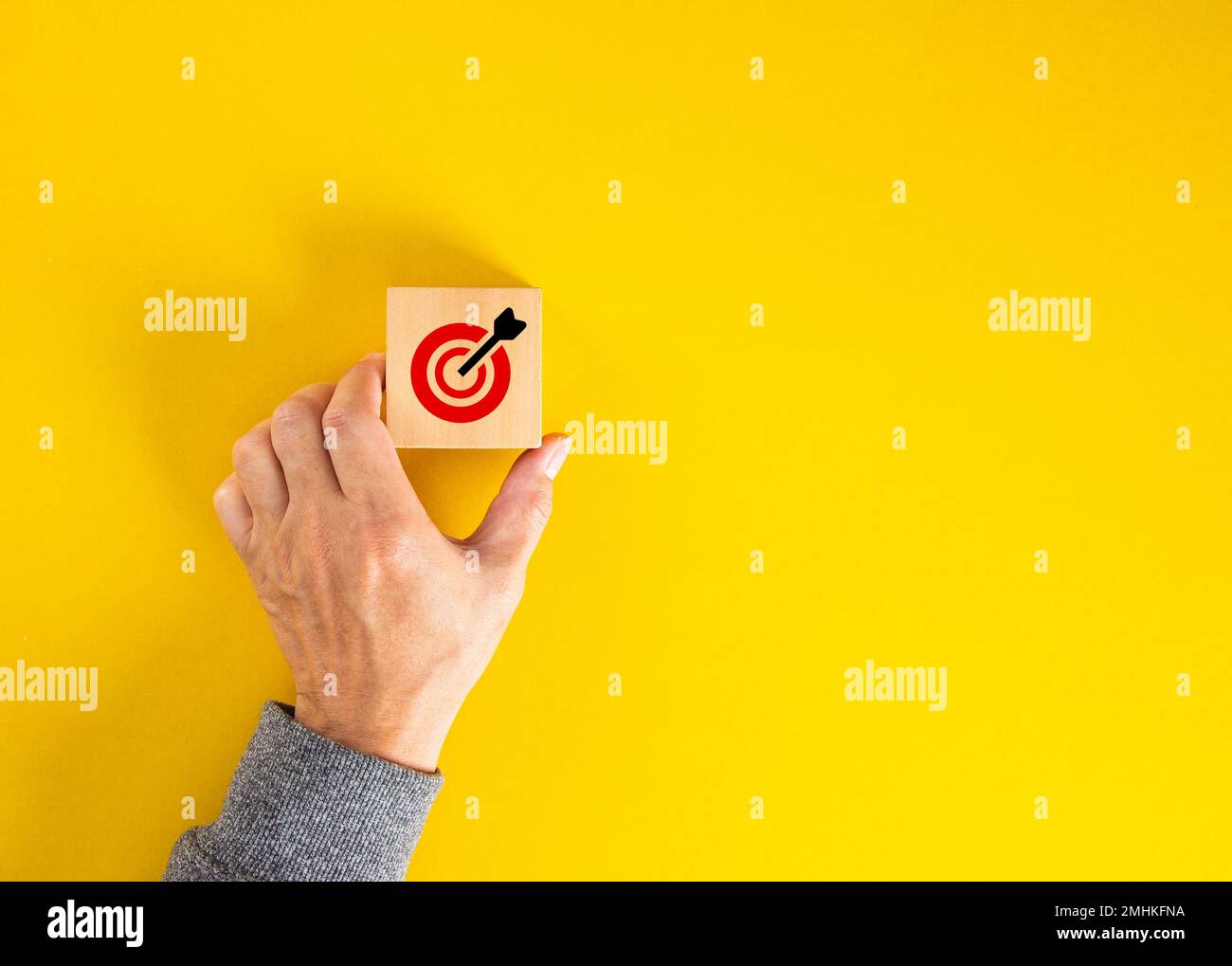 Hand, die einen Holzwürfel mit einem roten Ziel und einem Pfeil hält, der Ziele und Erfolg repräsentiert. Stockfoto