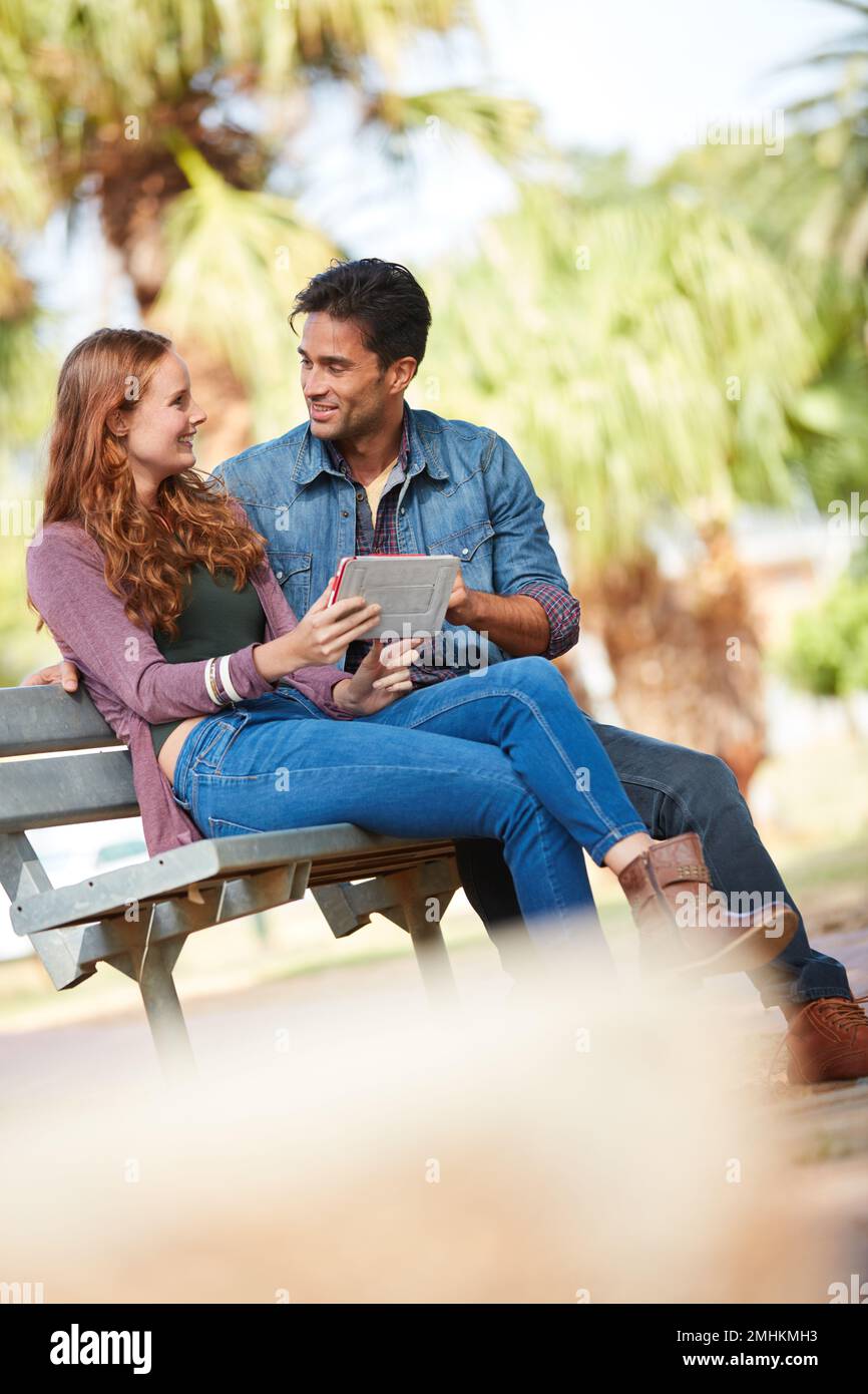 Unsere Herzen haben eine dedizierte WLAN-Verbindung zwischen ihnen. Ein junges Paar, das ein Tablet im Park benutzt. Stockfoto