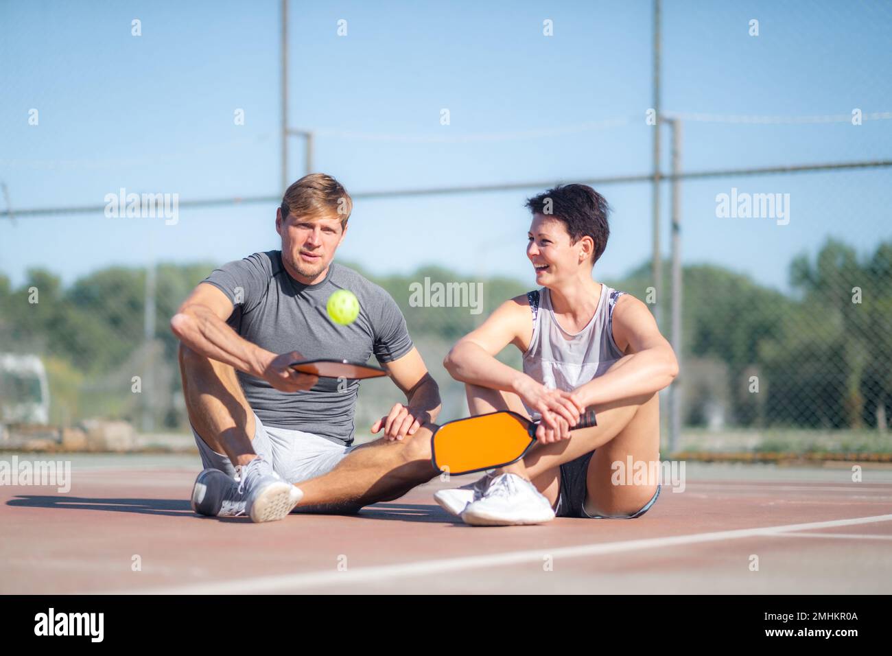 Pickleball-Spiel, entspannende Pickleball-Spieler mit gelbem Ball und Paddel-Sitzen nach dem Spiel, Outdoor-Sport-Freizeitaktivitäten. Stockfoto