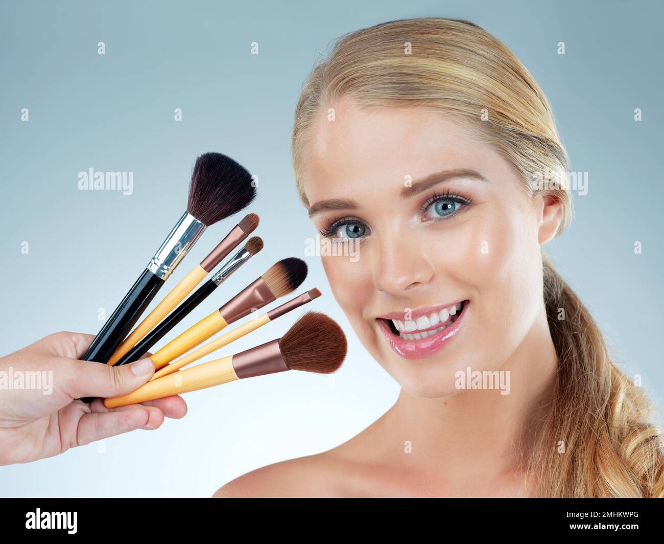 Ich habe die richtigen Werkzeuge. Studioporträt einer wunderschönen jungen Frau, die mit Make-up-Pinseln vor blauem Hintergrund posiert. Stockfoto