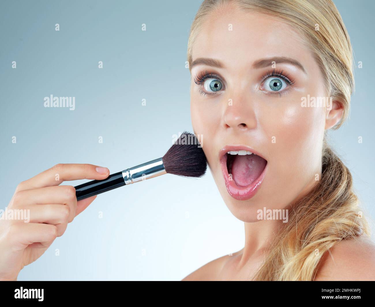Dieser Rotzlöffel wird Sie sprachlos machen. Studioporträt einer wunderschönen jungen Frau mit einem Make-up-Pinsel vor blauem Hintergrund. Stockfoto