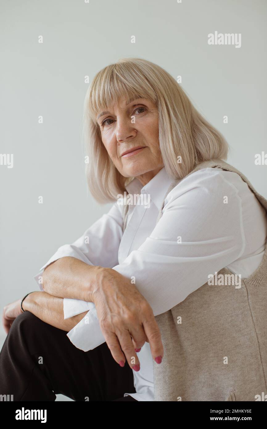 Studioporträt einer grauhaarigen Seniorin. Sie lehnt sich an Ellbogen, schaut in die Kamera. Stockfoto