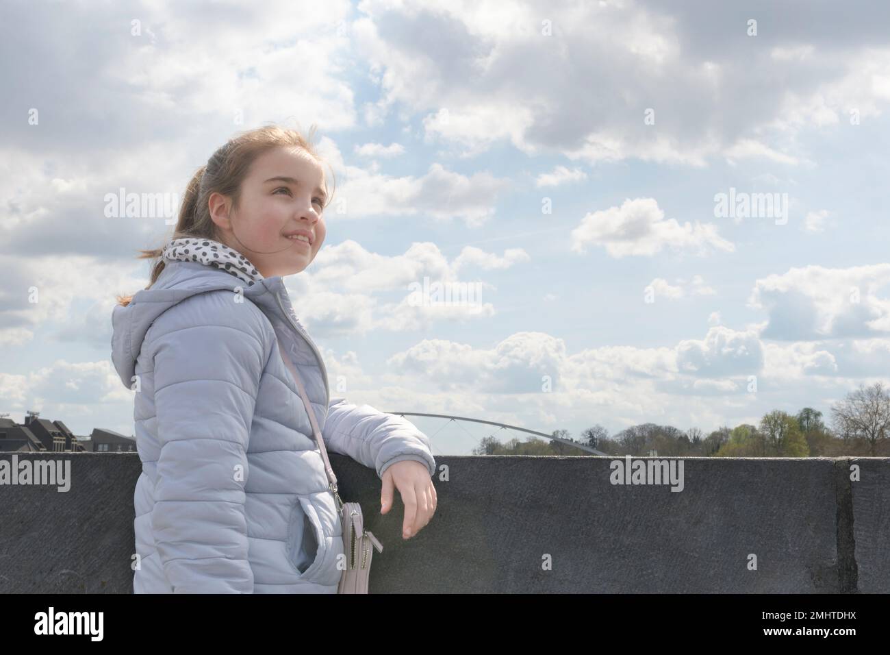 Frühlingsstimmung. Ein Mädchen im Teenageralter auf einem Spaziergang durch die Stadt vor dem Hintergrund eines wolkigen Frühlings-Himmels. Speicherplatz kopieren Stockfoto