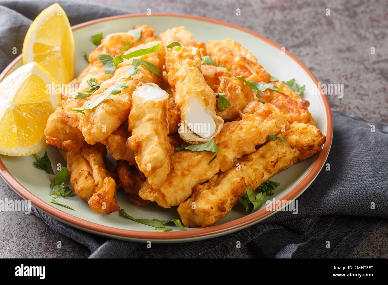 Frittierte panierte Calamari-Streifen mit Zitronennaht auf dem Teller auf dem Tisch. Horizontal Stockfoto