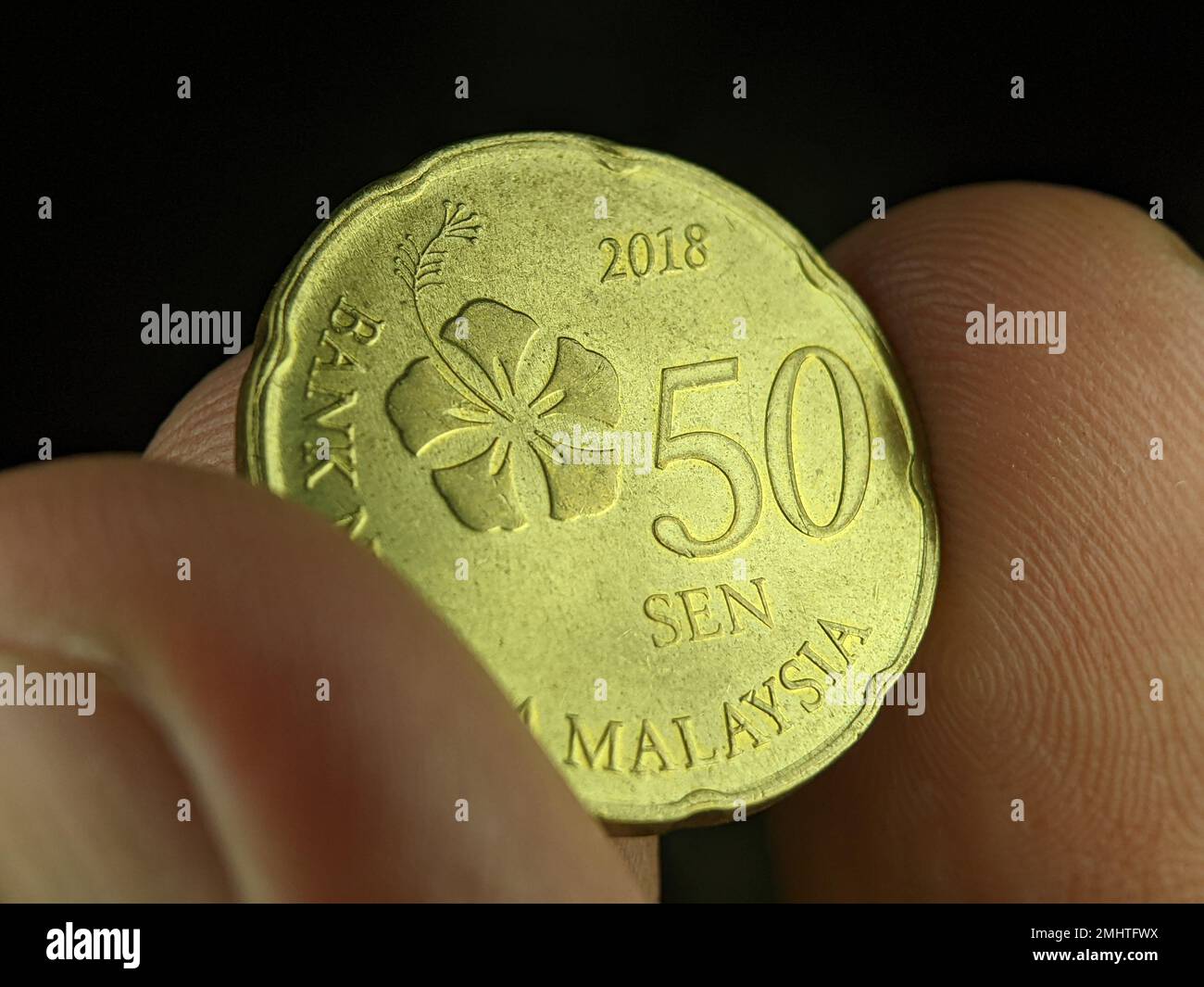 Zeigefinger mit 50-Cent-Münze aus Malaysia auf schwarzem Hintergrund. Stockfoto