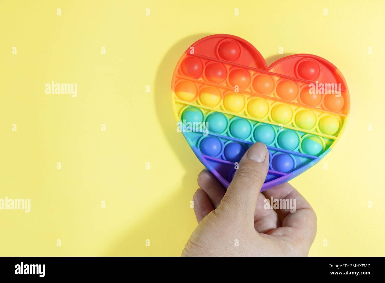 Farbenfrohes Anti-Stress-Spielzeug. Regenbogen-Sinnesfidget isoliert auf gelbem Hintergrund in der Hand während des Spiels. Spielzeug für die Entwicklung von Fine mot Stockfoto