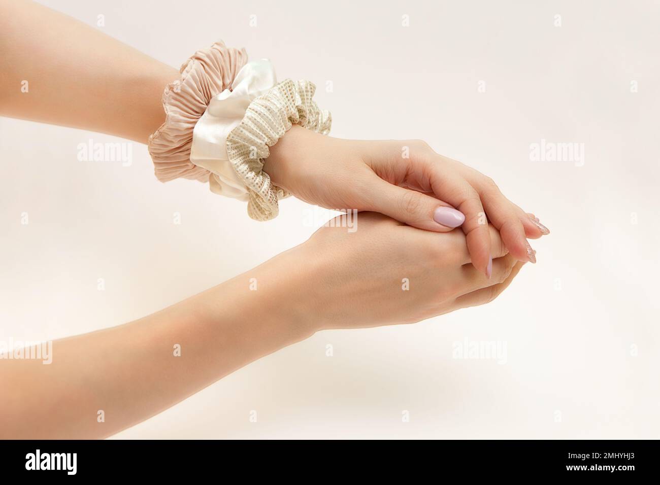 muscheln auf der Frauenhand. Elastische Seidenbänder am Frauenarm. Luxuriöse Beige- und Goldfarben. Haarband Stockfoto