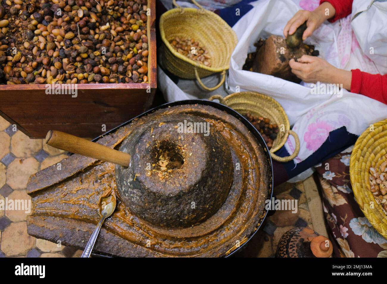Fez, Marokko - Draufsicht auf die Handmühle aus Arganöl, Kasten mit Samen, weibliche Hände, die auf die Nüsse schlagen. Arbeitsintensive Produktion mit traditionellem Mahlwerk. Stockfoto