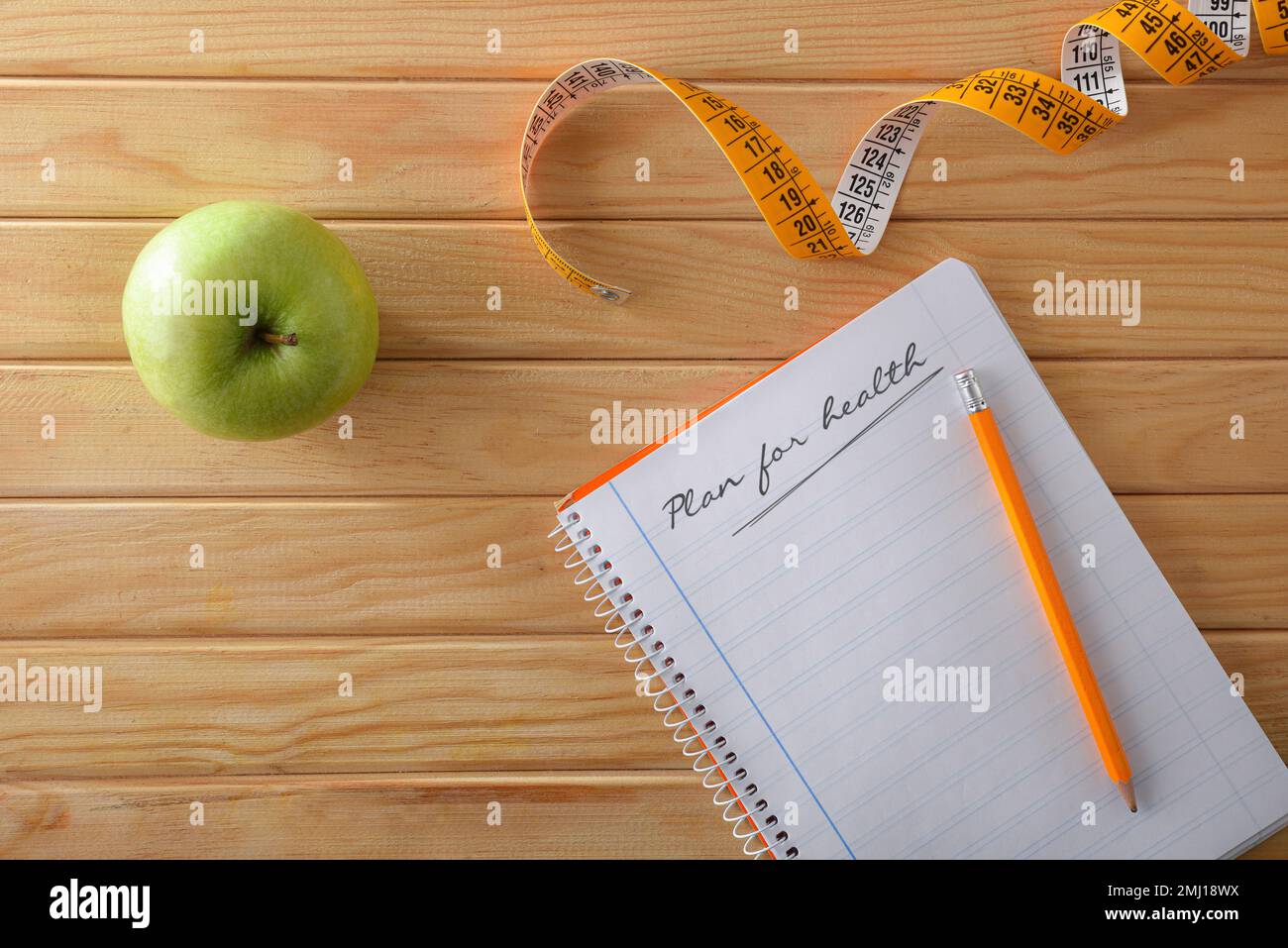 Gesundheitsplan mit Notizbuch und Bleistift auf Holztisch mit Apfel und Maßband. Draufsicht. Stockfoto