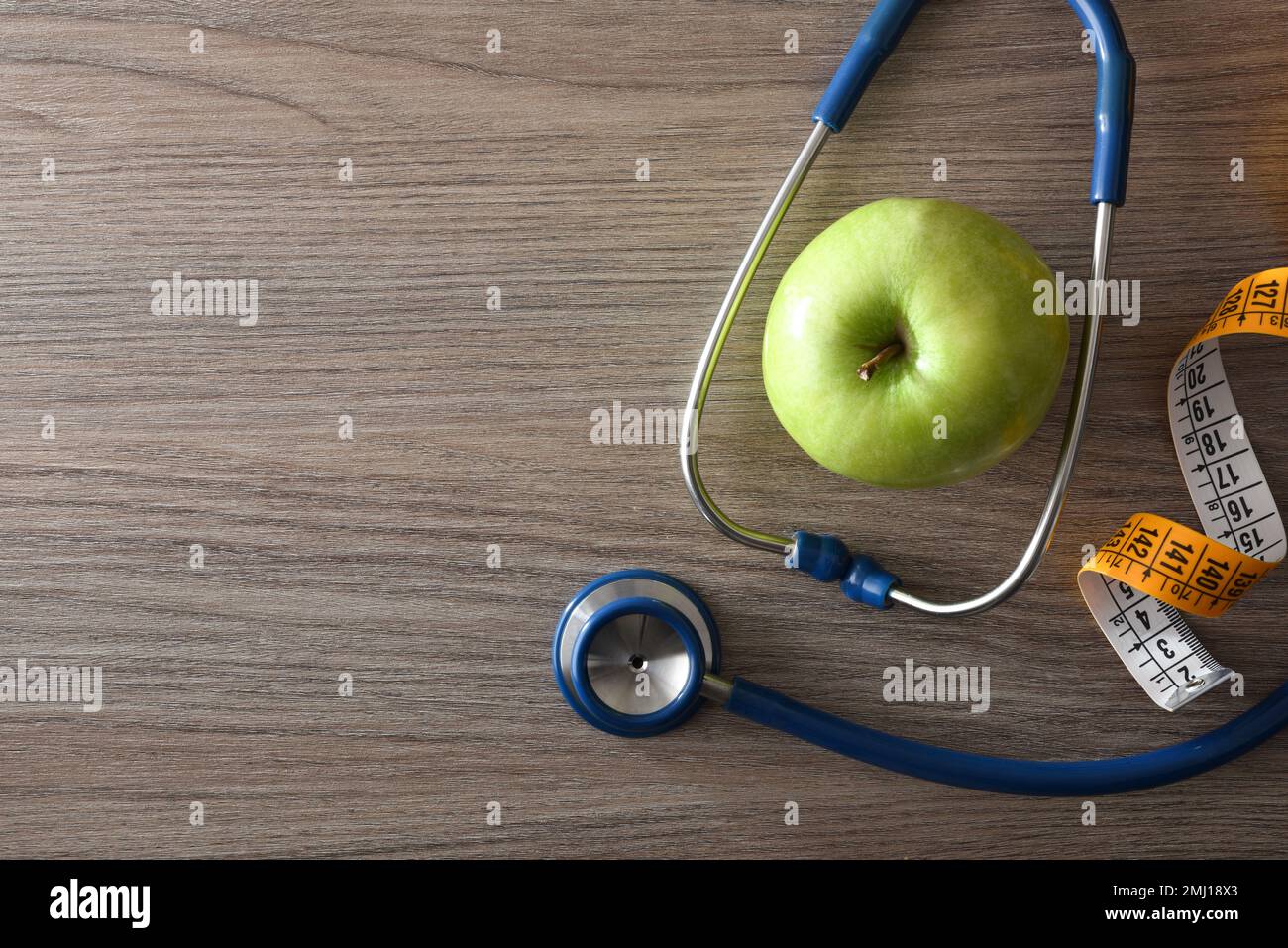 Gesundheitscheck und gesunder Lebensstil mit Apfel, Maßband und Stethoskop auf Holztisch. Draufsicht. Stockfoto