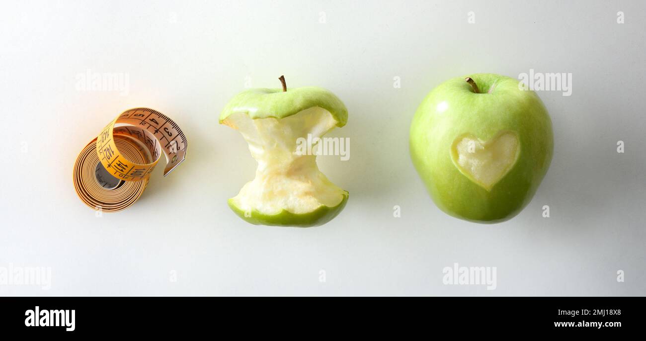 Konzept der gesunden Ernährung und Gewichtskontrolle mit Apfel mit Herz und halb gefressenem Apfel und Maßband daneben auf weißem Tisch. Draufsicht. Stockfoto