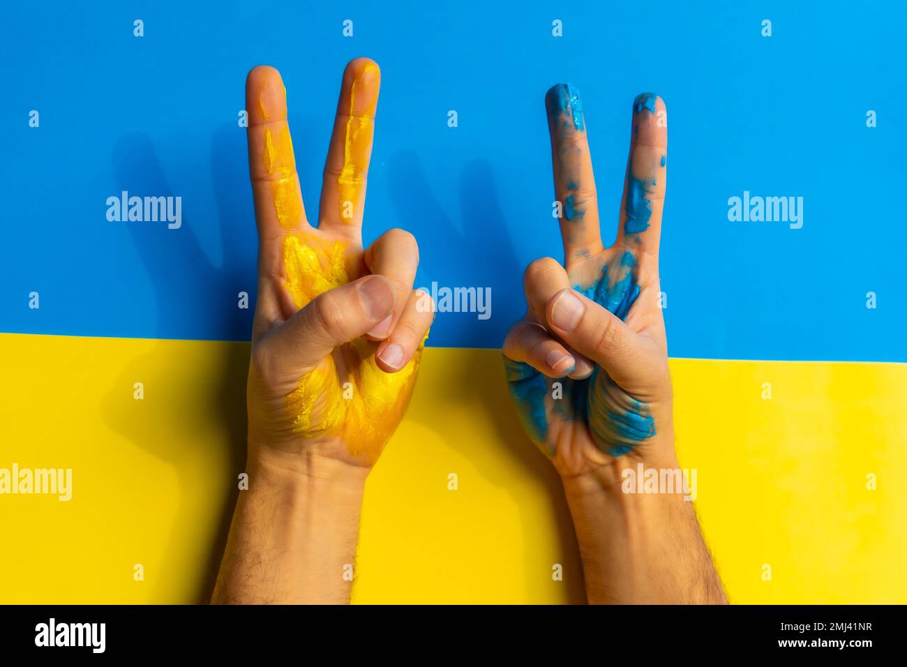 Beenden Sie den Krieg, den Konflikt zwischen der Ukraine und Russland. Ein Mann, der die Farben der ukrainischen Flagge trägt und das Siegeszeichen macht Stockfoto