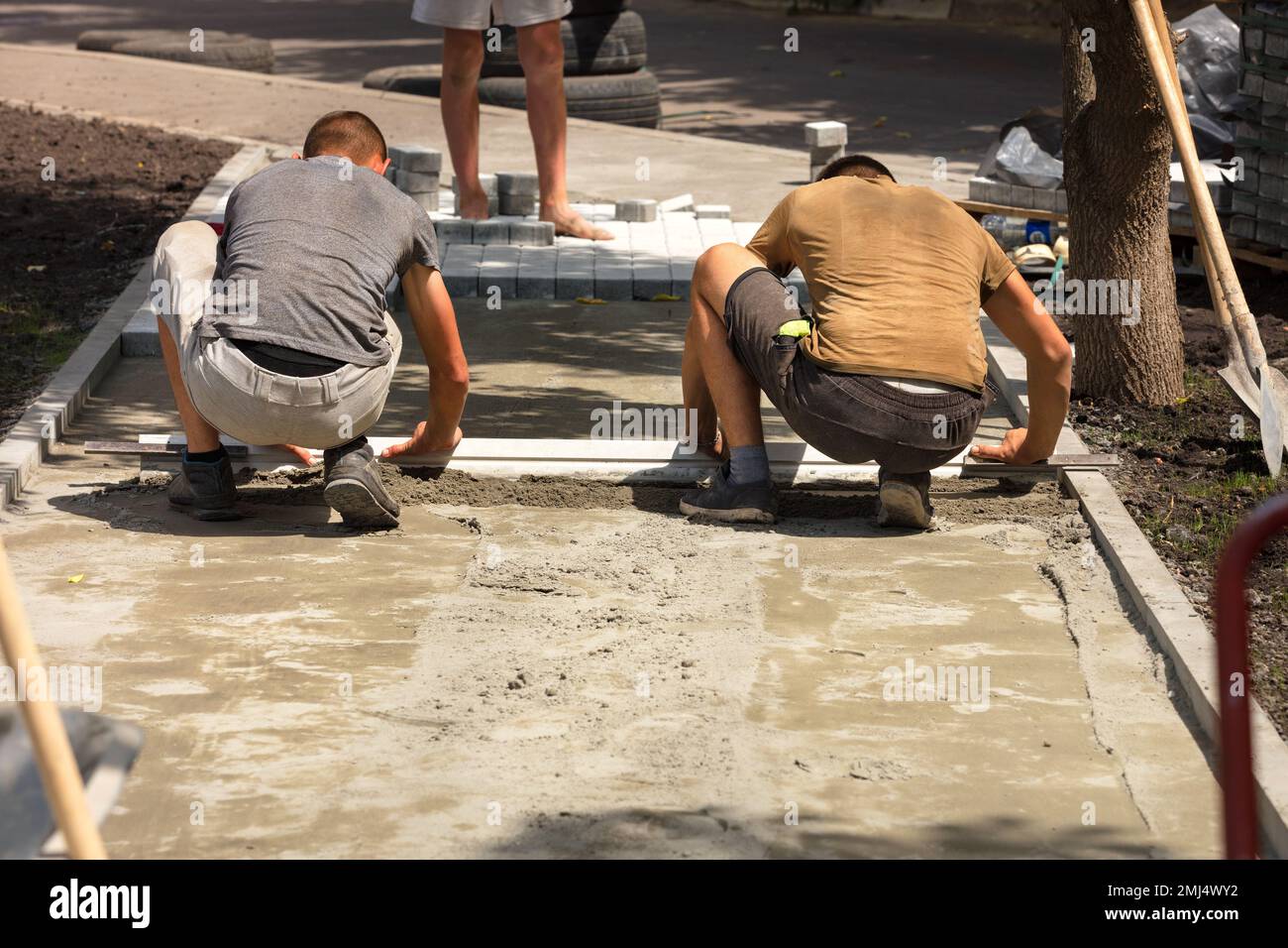 Junge Arbeiter machen einen Weg, legen Pflasterplatten auf Sandbasis an einem hellen, sonnigen Tag. Speicherplatz kopieren. Stockfoto
