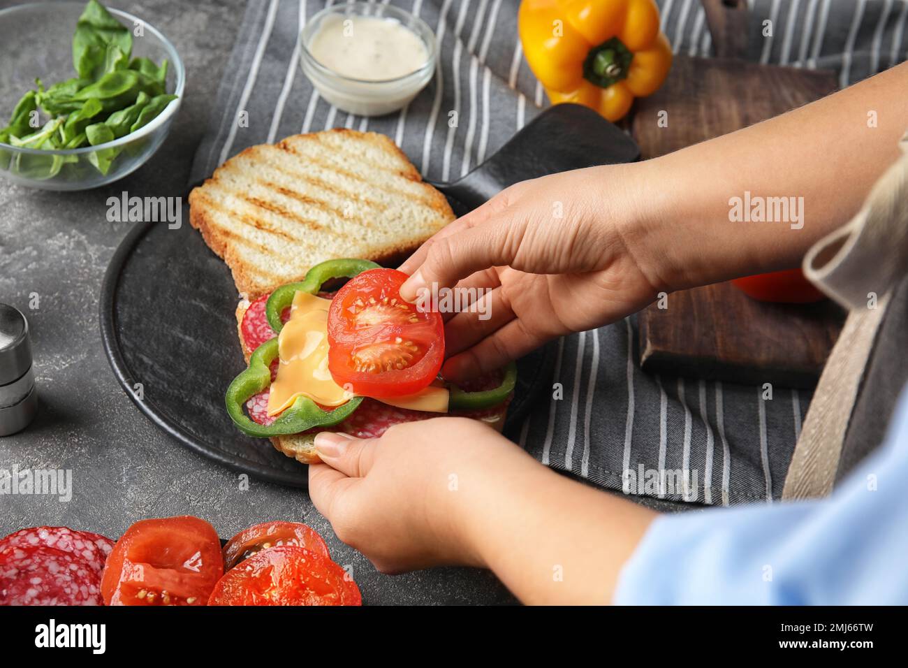 Frau, die Tomaten zum Sandwich am grauen Tisch hinzufügt, Nahaufnahme Stockfoto