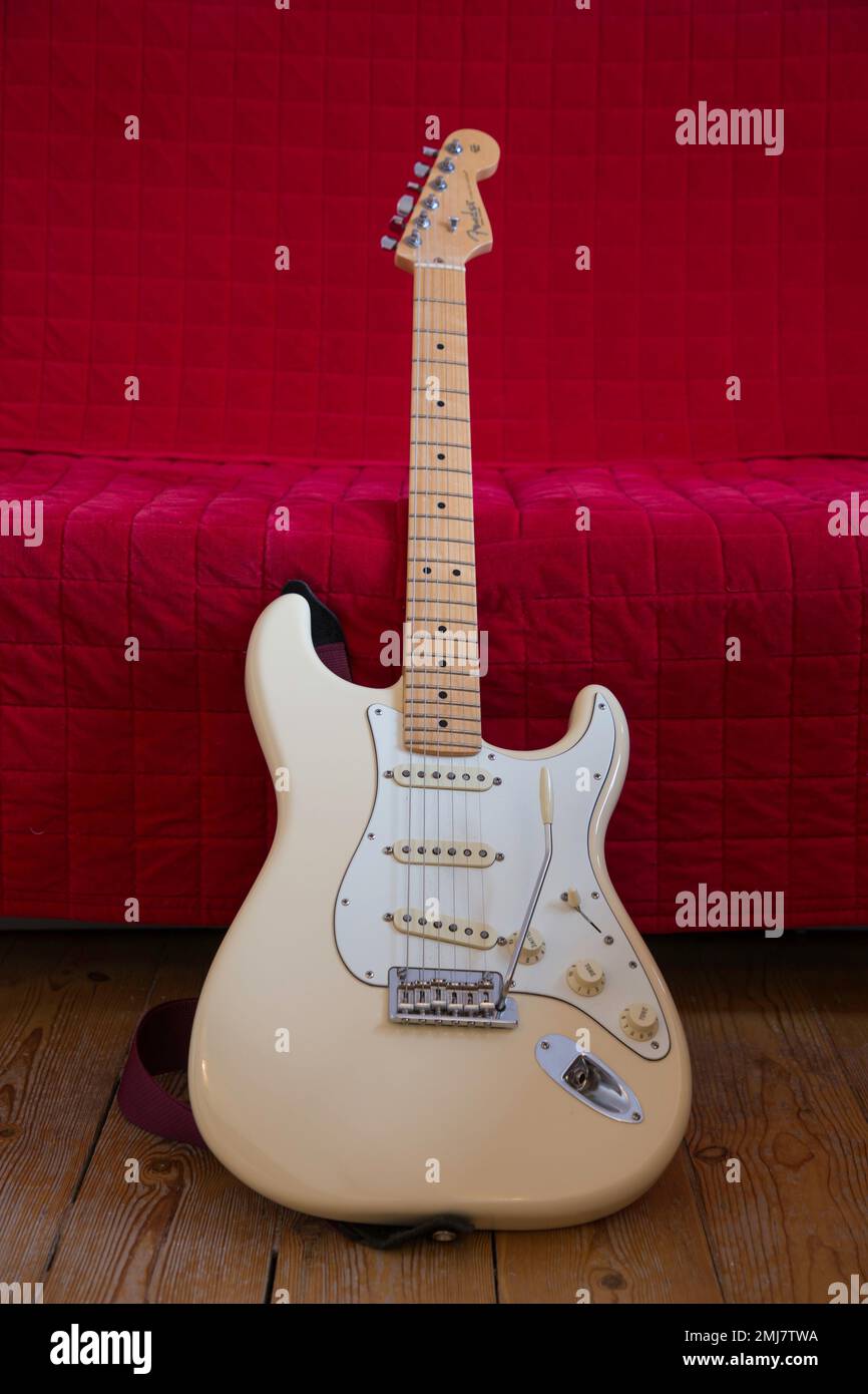 Weißer amerikanischer Fender Stratocaster lehnt sich auf ein rotes Sofa Stockfoto