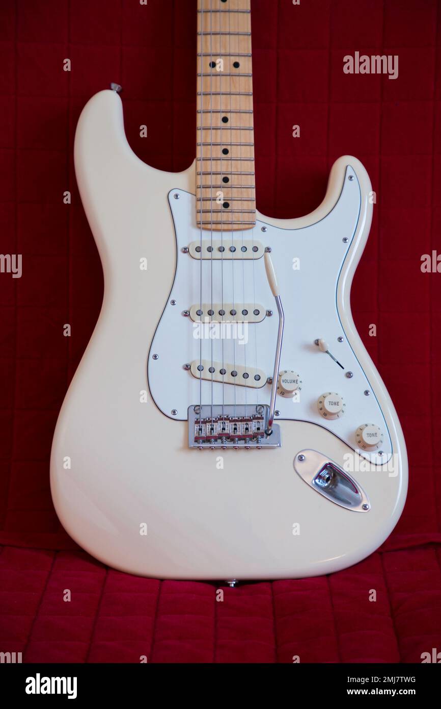 Weißer amerikanischer Fender Stratocaster lehnt sich auf ein rotes Sofa Stockfoto