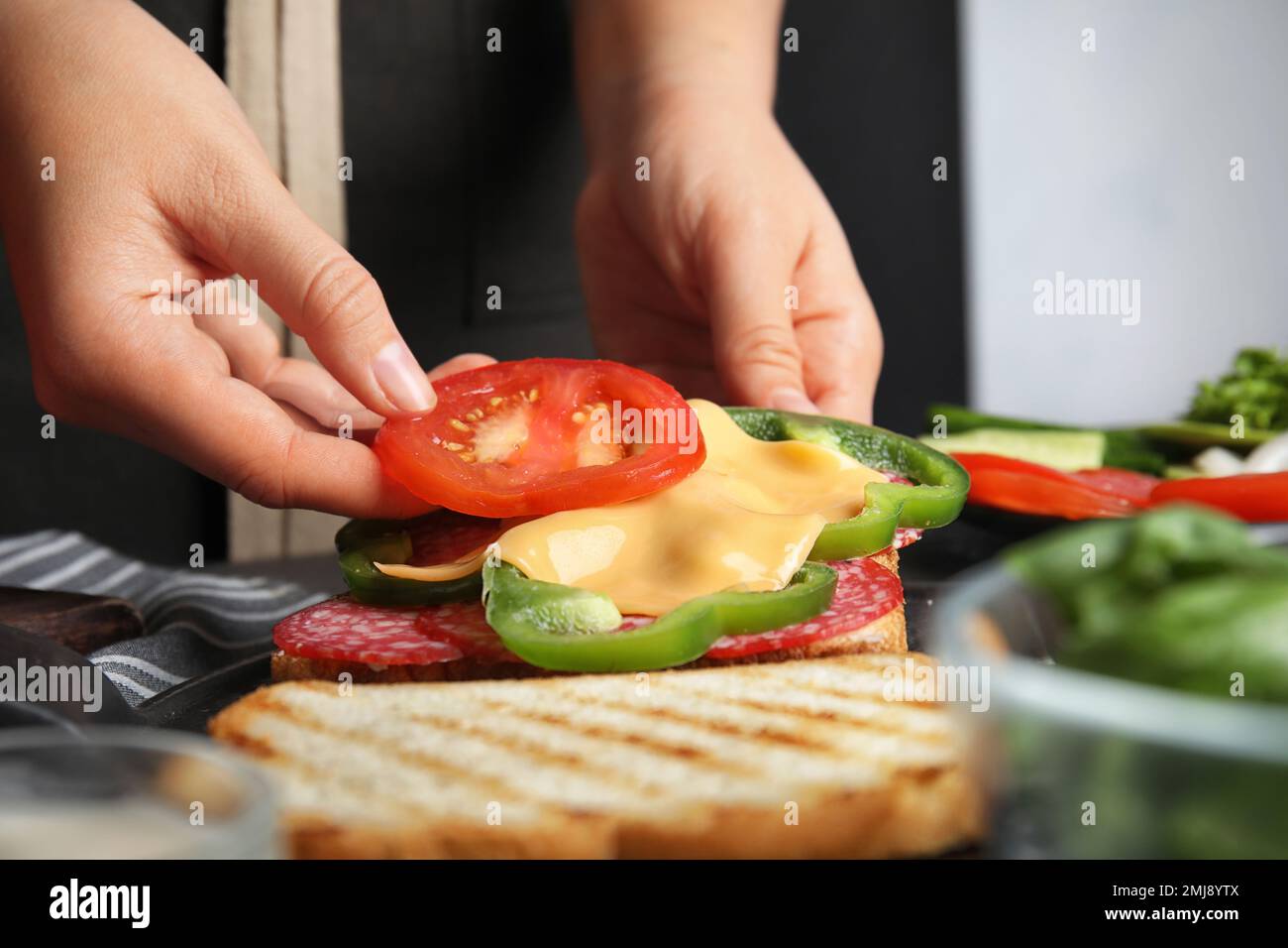 Frau, die Tomaten zum Sandwich am Tisch hinzufügt, Nahaufnahme Stockfoto