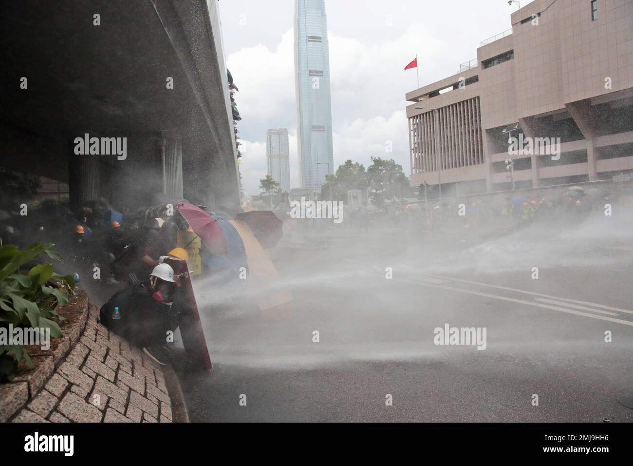 Protestors take cover from water cannon in central Hong Kong, Saturday, Aug. 31, 2019. Hong Kong police fired blue-colored water from water cannons and tear gas on Saturday in a standoff with protesters outside government headquarters. (AP Photo/Jae C. Hong) Stockfoto