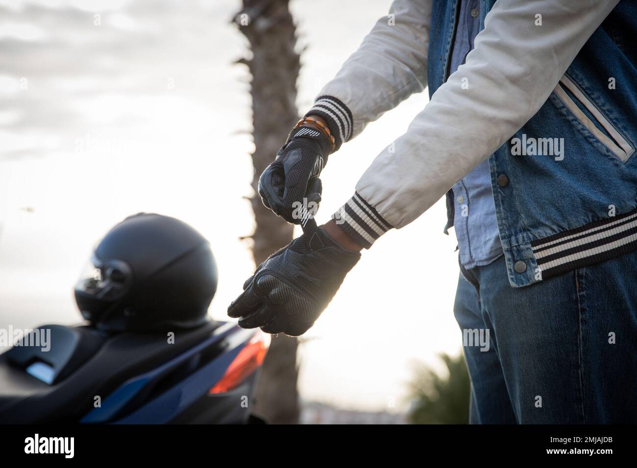 Die Hand eines Bikers, der Handschuhe anzieht, während der Roller mit Helm auf der Seite geparkt ist Stockfoto