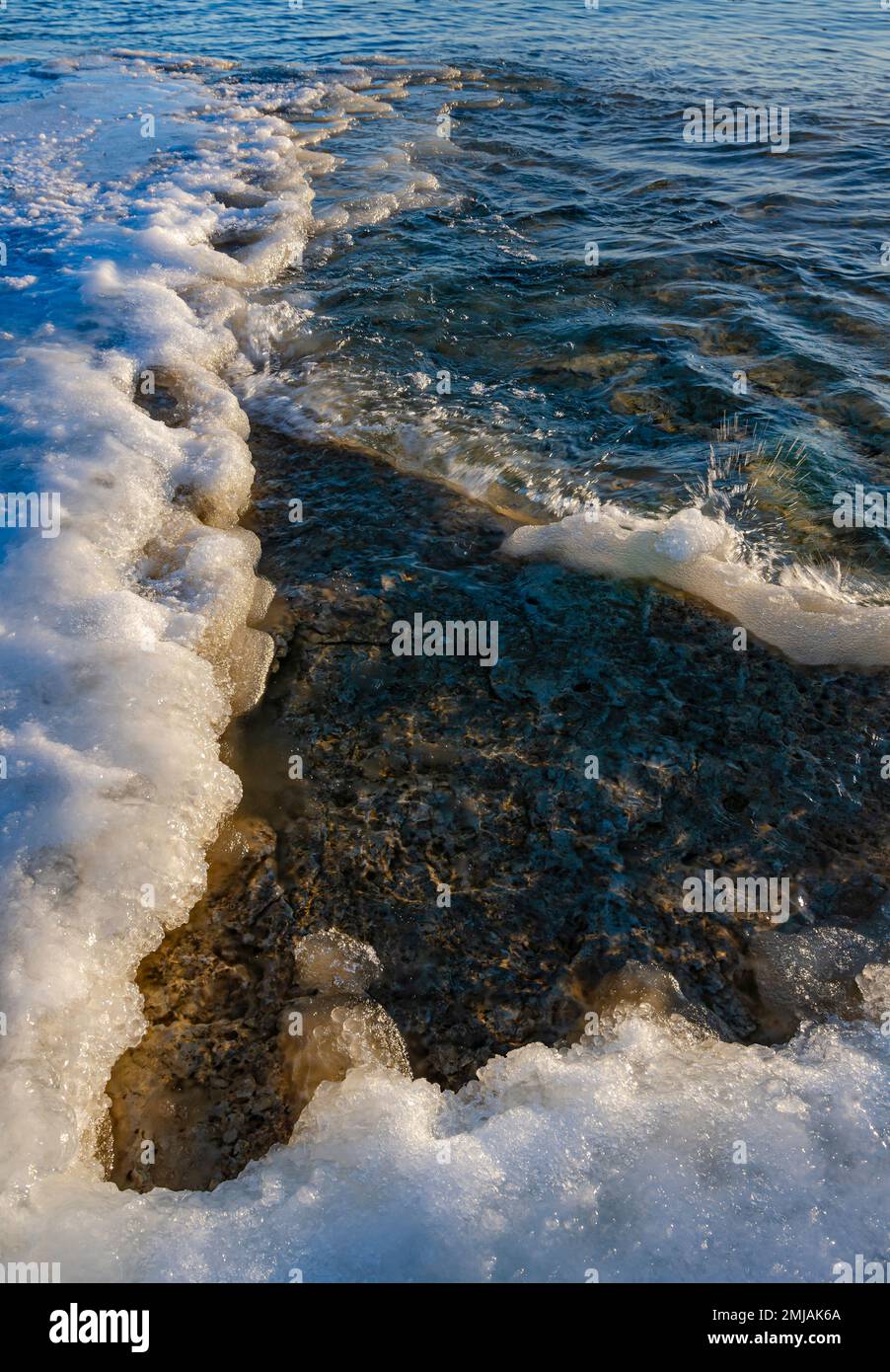 Sanfte Wellen schlängeln sich auf dem Eis der Küste und erzeugen kleine Wasserspritzer, die in das warme Licht am frühen Morgen, Cave Point County Park, Door, aufprallen Stockfoto