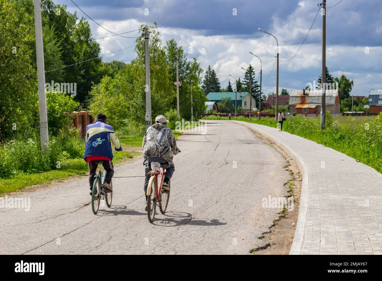 Vorsino, Russland - Juli 2017: Arbeitende Gastarbeiter, die mit dem Fahrrad ins Dorf fahren Stockfoto