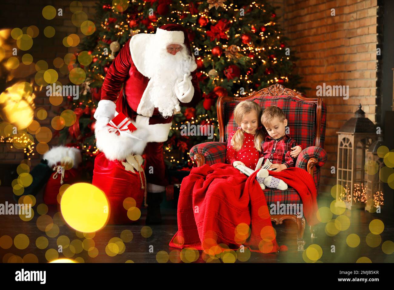 Der Weihnachtsmann schleicht sich mit Geschenken herein, während Kinder in der Nähe des Weihnachtsbaums im Haus Bücher lesen Stockfoto