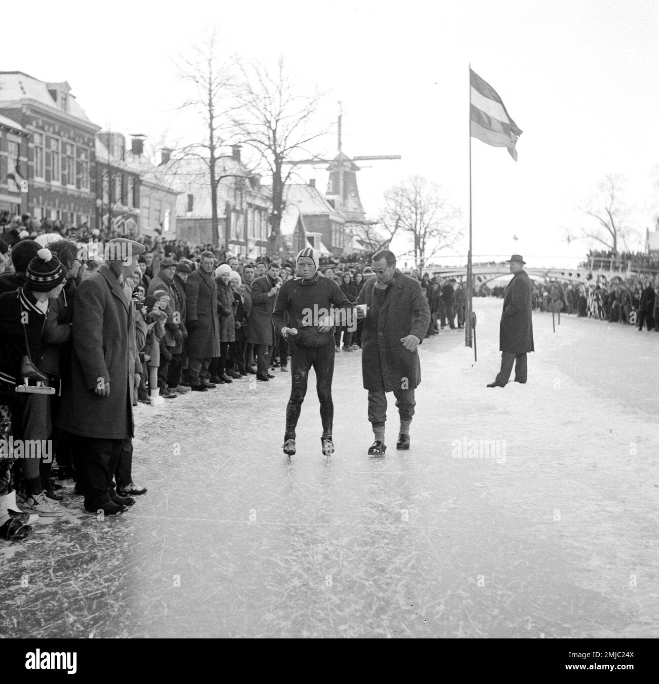 Niederländische Geschichte: Menschenmassen versammelten sich, um die Elfstedentocht zu beobachten, ein Teilnehmer auf der Seite des Eiss ca. Januar 1963 Stockfoto