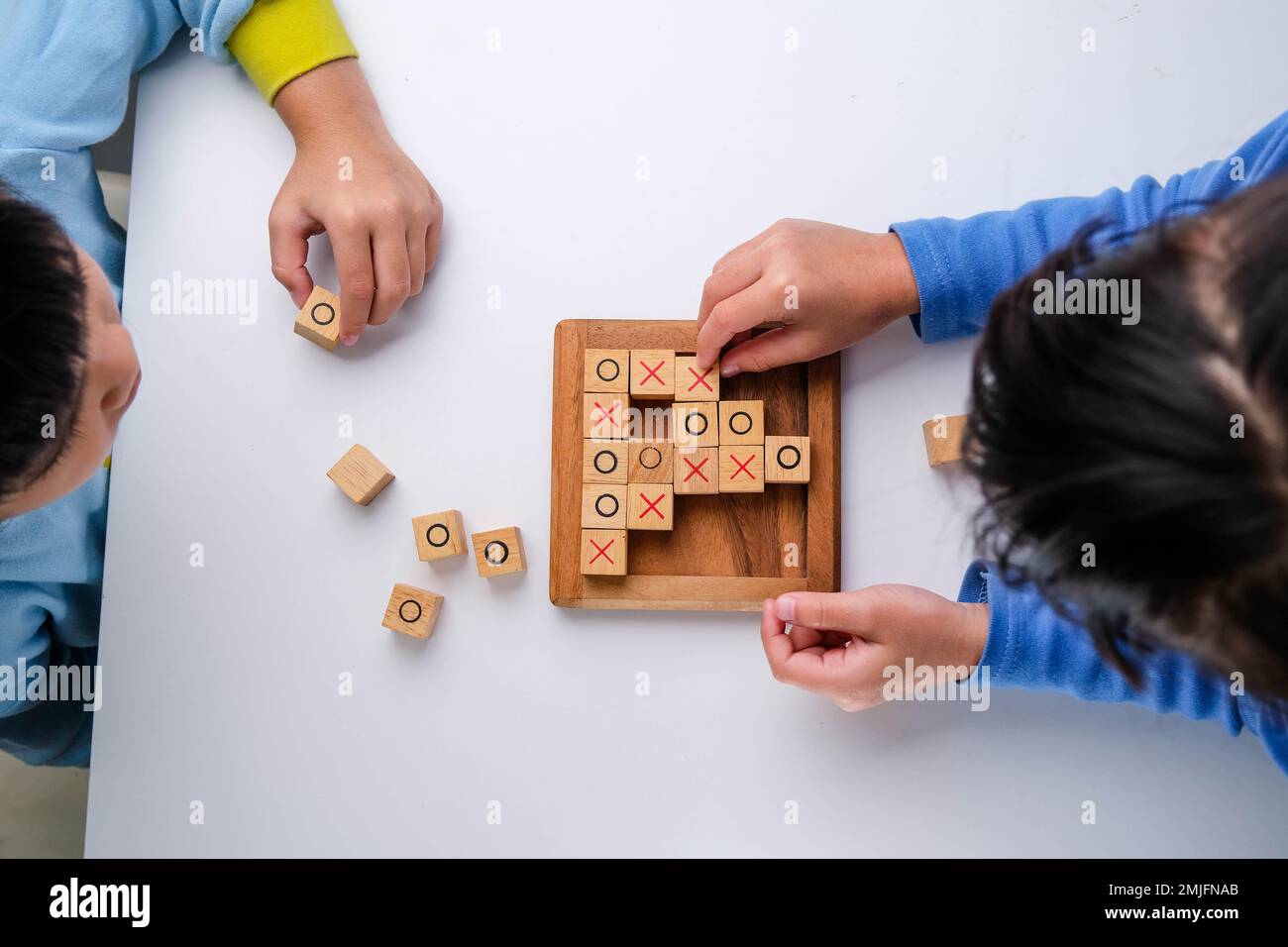 Kleine Geschwister spielen Holzbrettspiel Tic-tac-Toe auf dem Tisch im Wohnzimmer. Die Familie verbringt am Wochenende Zeit miteinander. Stockfoto