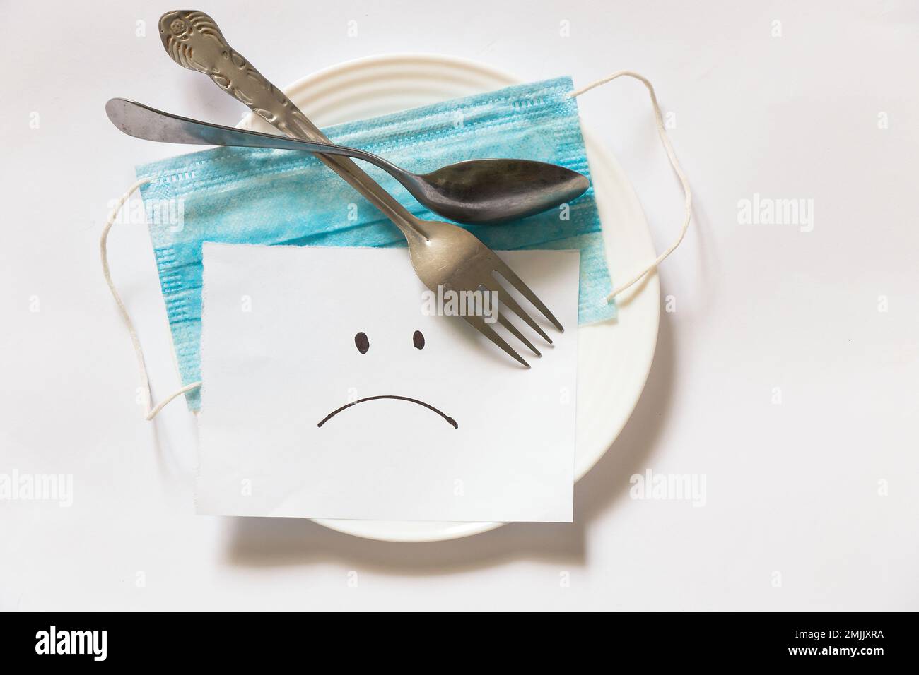 Medizinische Maske ein trauriges Smiley wird auf weißem Papier auf einem weißen gezeichnet Stockfoto