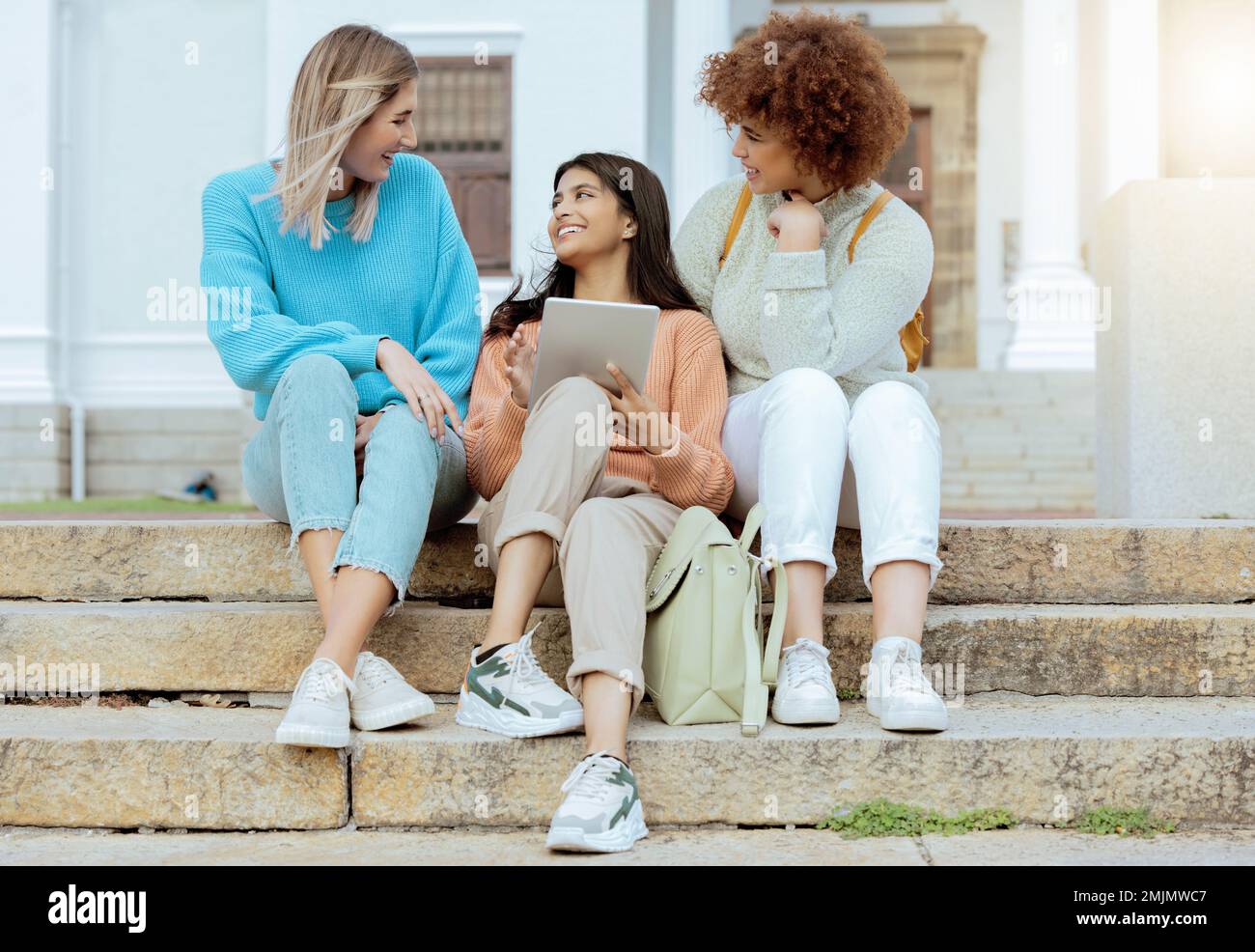 Schüler, Freunde und Tablet auf Treppen in Konversation, sozialen Medien oder Kommunikation auf dem Campus. Glückliche Frauen, die gerne diskutieren, sich unterhalten oder mit ihnen sprechen Stockfoto