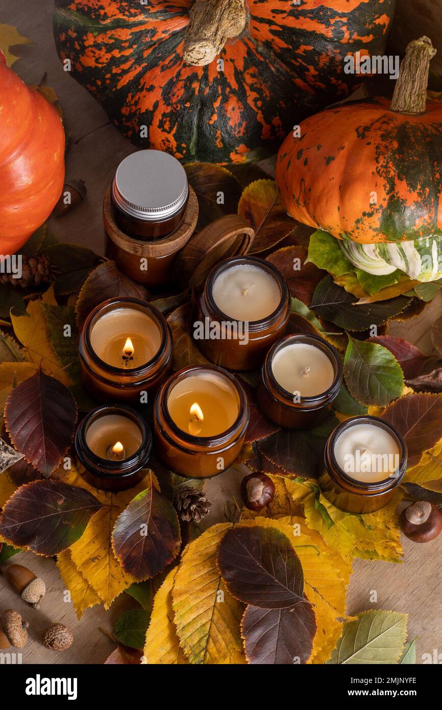 Sojalkerzen brennen in Gläsern. Baumblätter, Kürbis. Komfort zu Hause. Kerze in einem braunen Glas. Duft und Licht. Handgemachte Duftkerze. Aromatherapie. Herbststimmung. Gemütliches Wohndekor im Herbst. Stockfoto