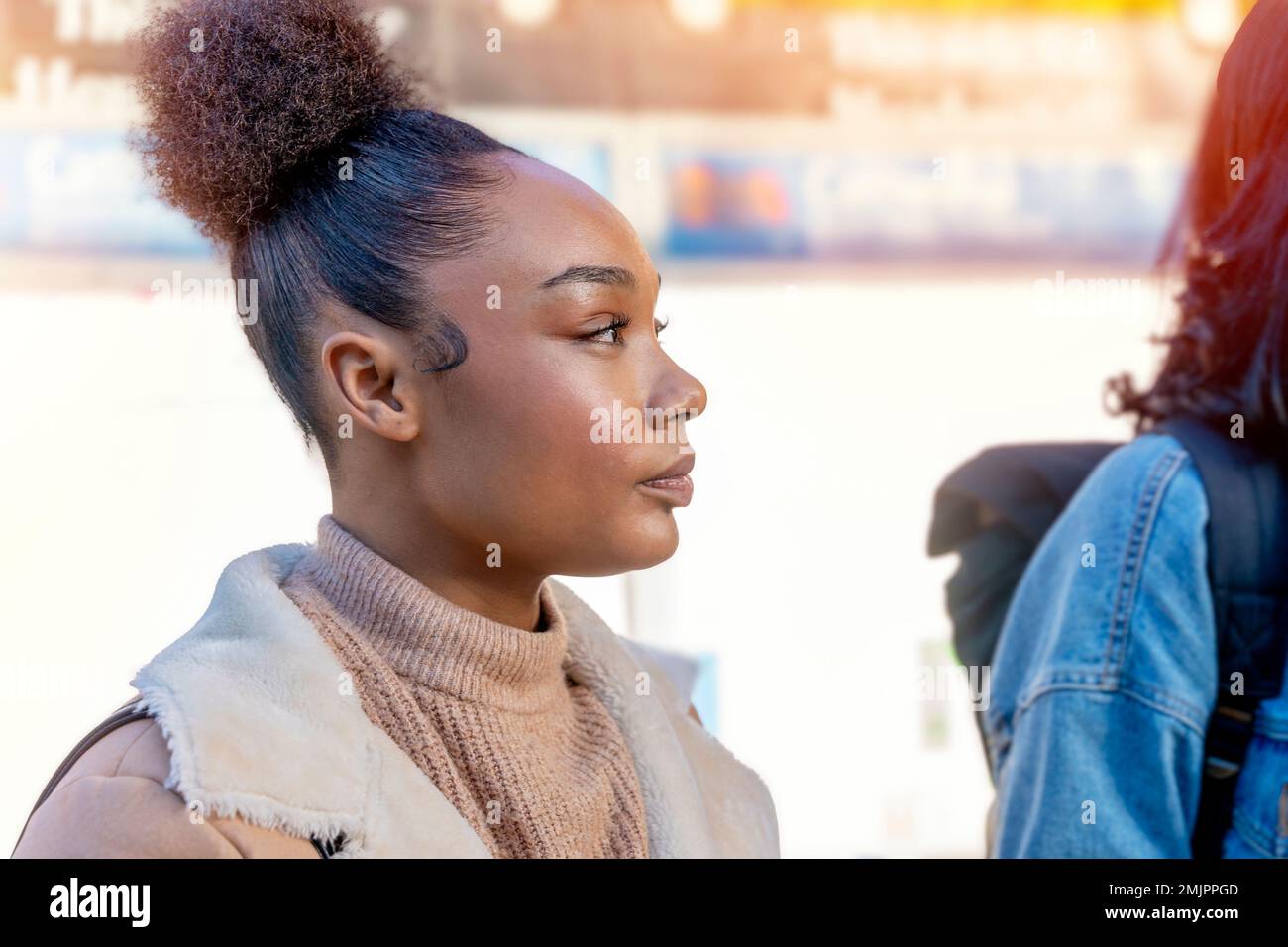 Fröhliche Afrikanerin hält eine Tasse Kaffee. Eine lächelnde braune Dame in braunem Pullover, die auf eine Straßenbahn wartet. Stockfoto