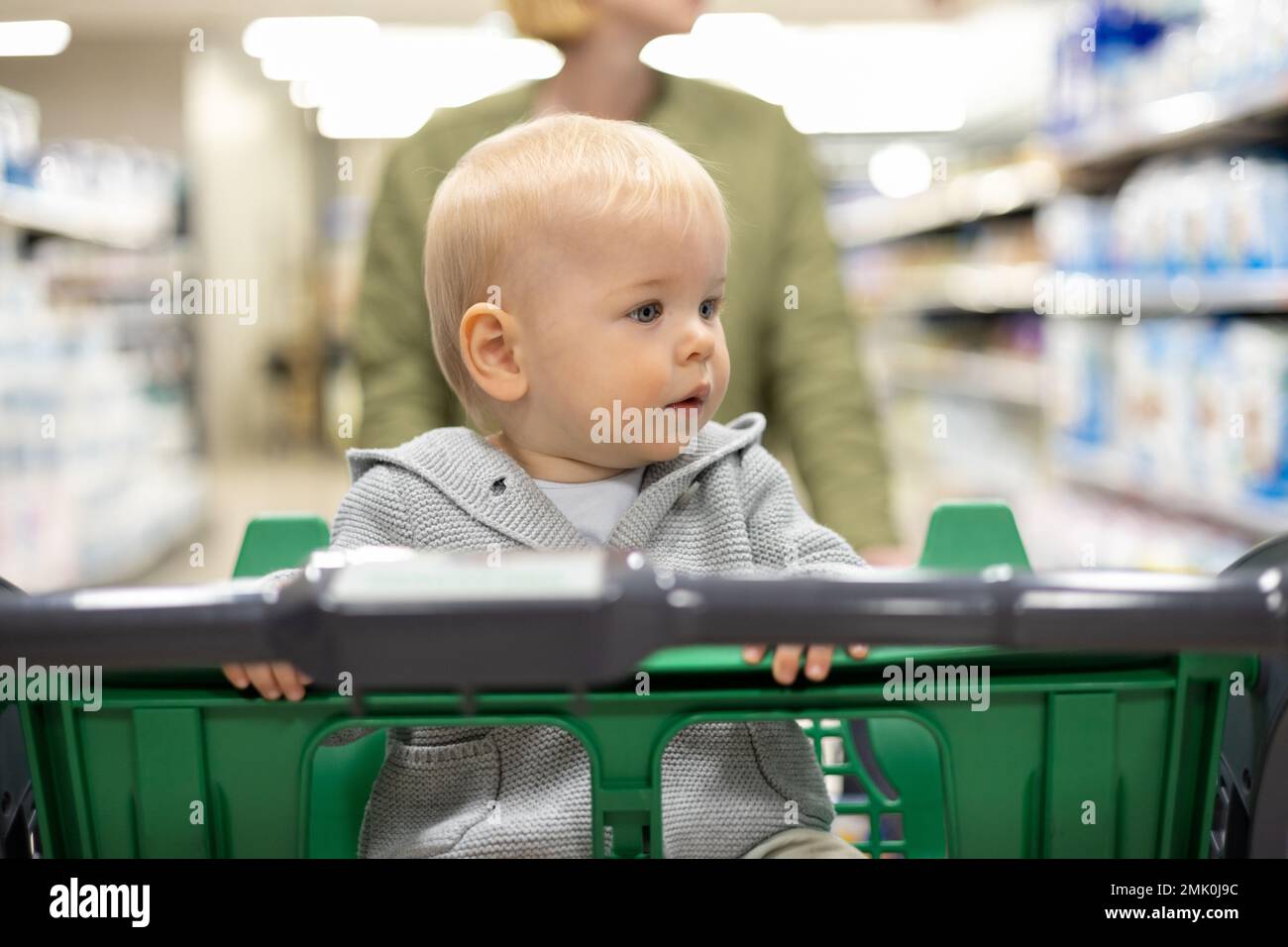 Mutter schiebt den Einkaufswagen mit ihrem kleinen Jungen durch die Abteilung im Supermarkt. Einkaufen mit Kindern Konzept Stockfoto