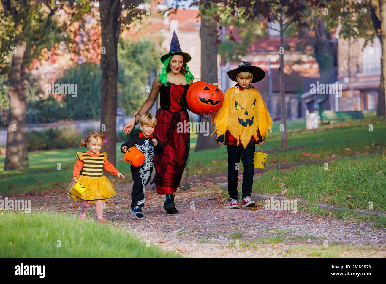 Mutterspaziergang mit Kindern in Halloween-Kostümen Eimer halten Stockfoto