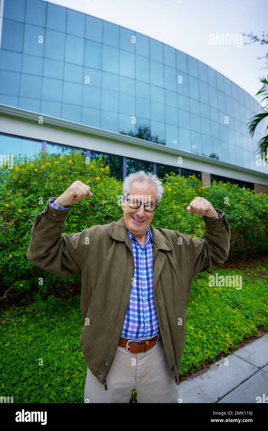 Ein älterer Mann, der seine Muskeln an einem Bürogebäude anlegt Stockfoto