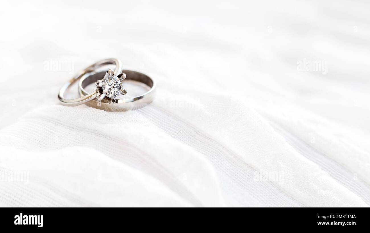Ein Paar goldene Eheringe auf weißem Textilhintergrund mit Kopierbereich. Verlobungsring mit Diamant auf Textilhintergrund. Symbol für Liebe und Ehe Stockfoto