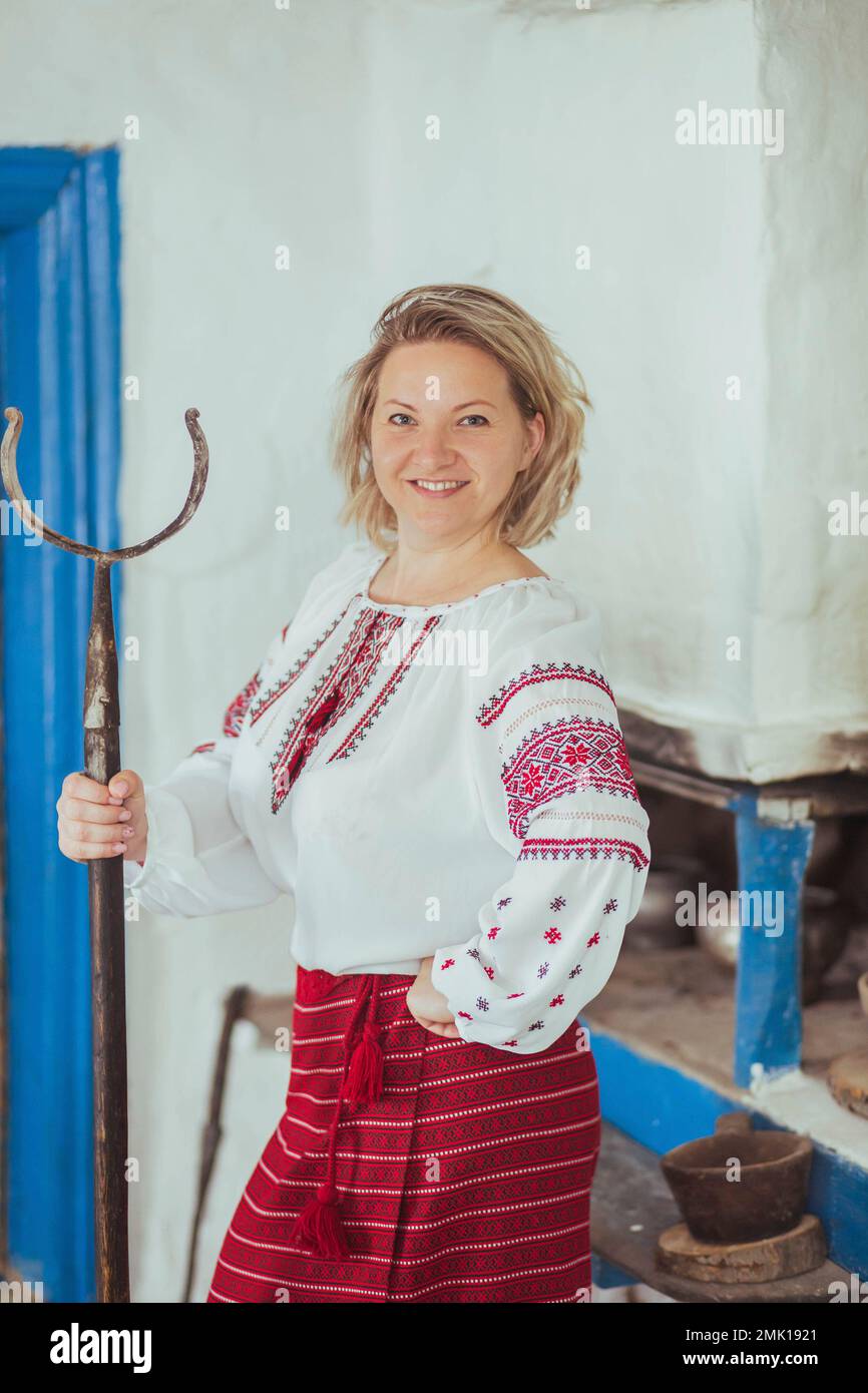 Hostess in bestickter Kleidung mit Poker in der Nähe des Ofens. Stockfoto