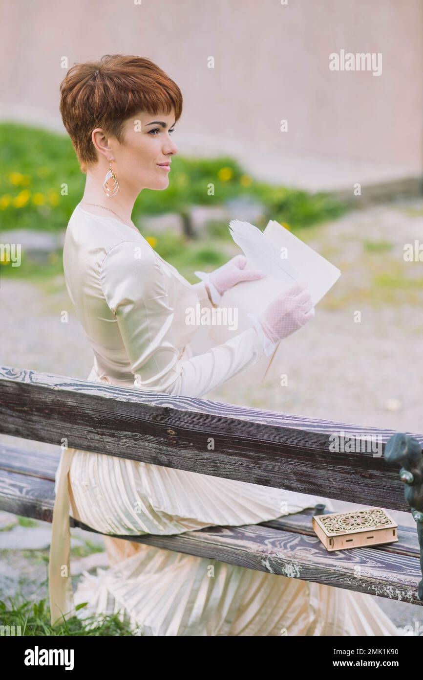Eine Frau in goldenem Kleid, die im Garten einen Brief mit Federstift schreibt Stockfoto