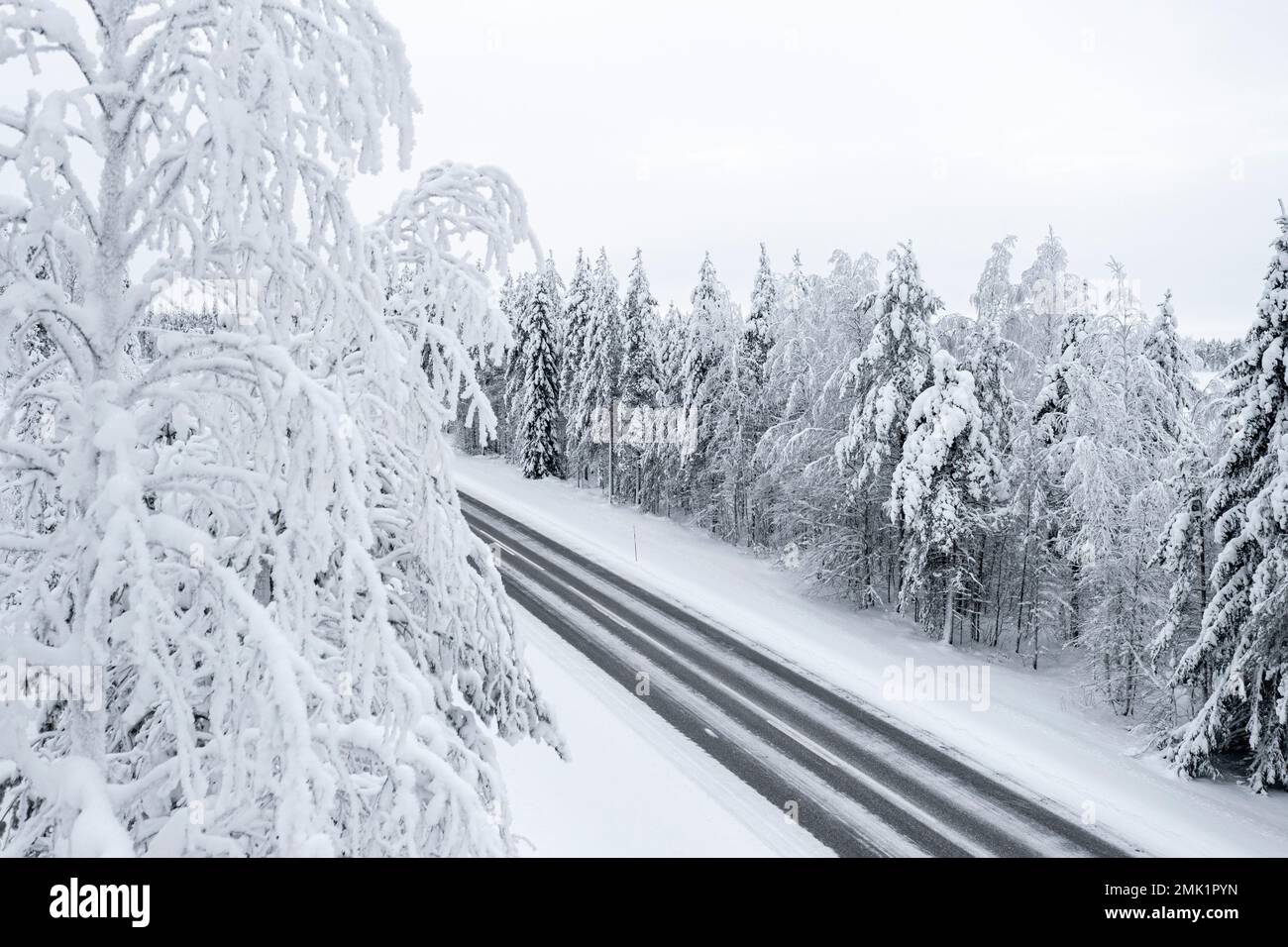 Eisige Straße inmitten des gefrorenen, verschneiten Waldes, Lappland, Finnland Stockfoto
