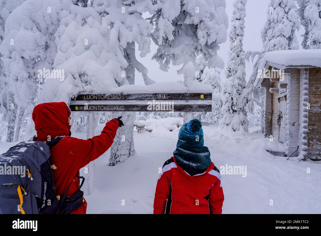 Fröhliche Mutter und Sohn, die auf einem Winterpfad eine verschneite Berghütte bestaunen, ISO Syote, Nordöstrobothnia, Lappland, Finnland Stockfoto