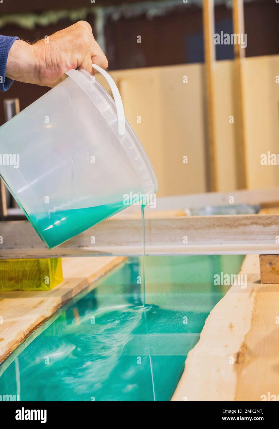 Zimmermann gießt türkisfarbenes Epoxid auf einen Küchentisch in der Werkstatt Stockfoto