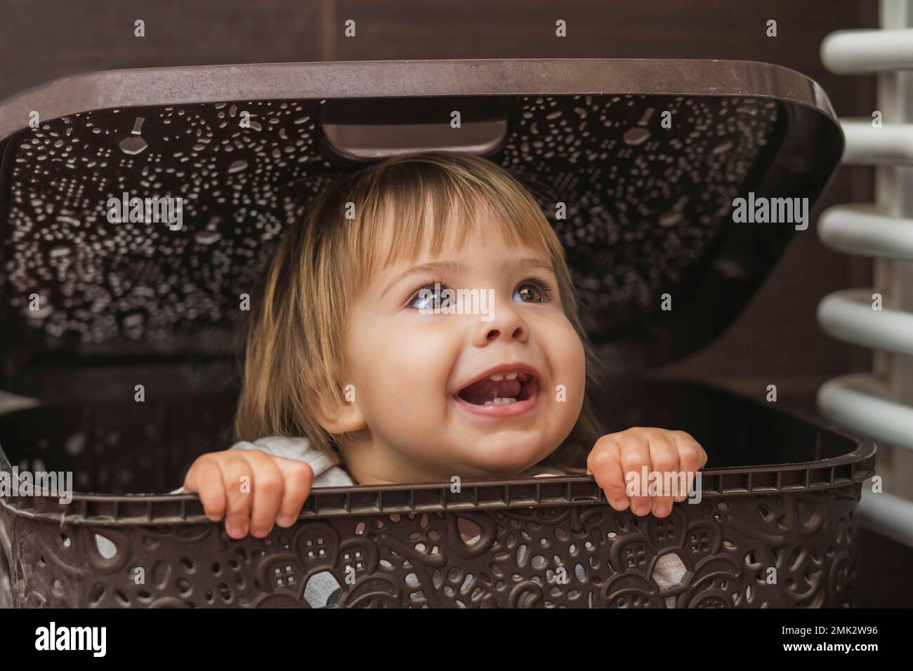 Süßes Baby, das sich in einem Wäschekorb versteckt Stockfoto