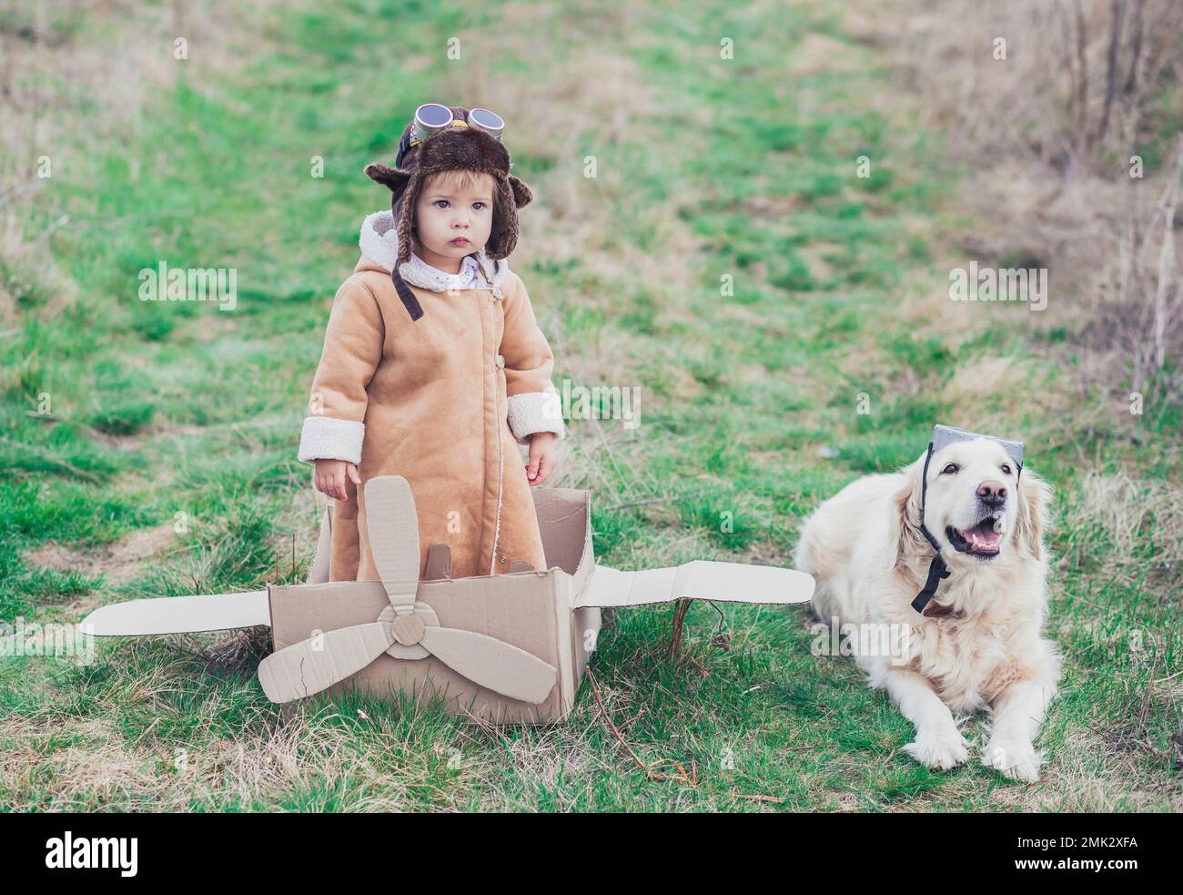 Baby in Pilotenkleidung und sein Co-Pilot in der Nähe des Pappflugzeugs Stockfoto
