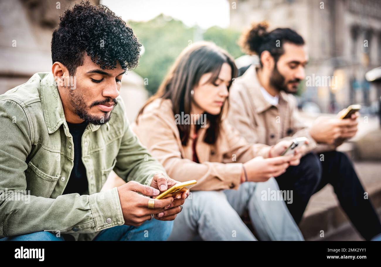 Städtische Personengruppe, die ein Smartphone benutzt und auf dem Hof einer Universität sitzt - Junge Freunde, die von Smartphone-Geräten abhängig sind Stockfoto