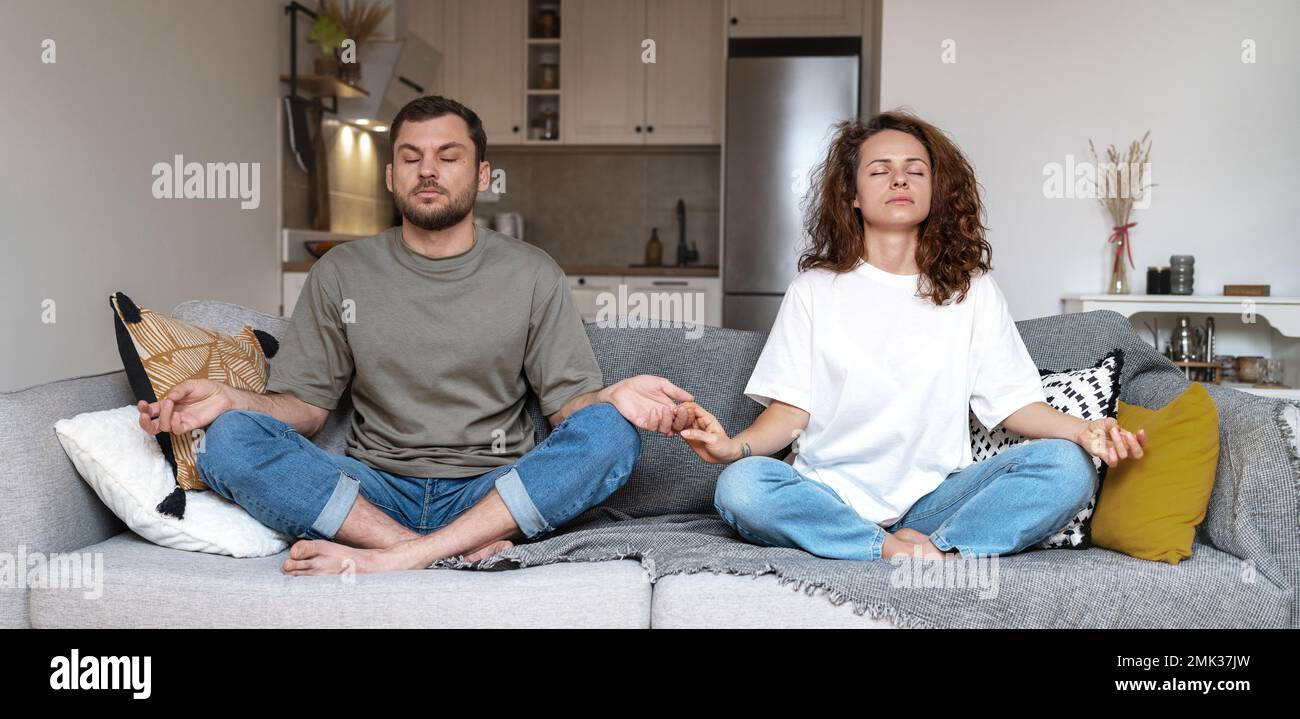 Ein Paar meditiert zusammen, während es zu Hause auf dem Sofa in Lotus posiert. Stockfoto